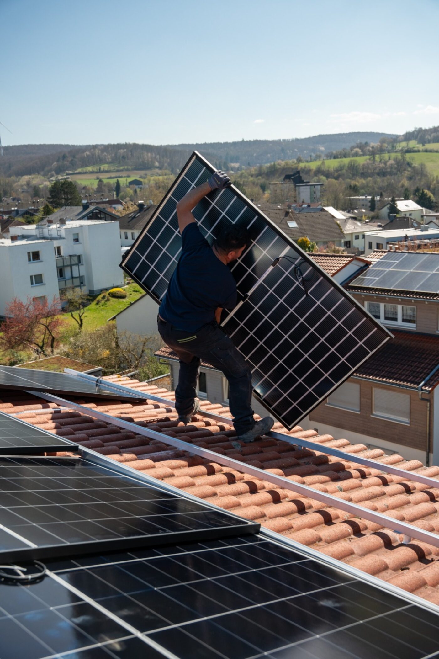 Monteur trägt Solarmodul über ein Ziegeldach